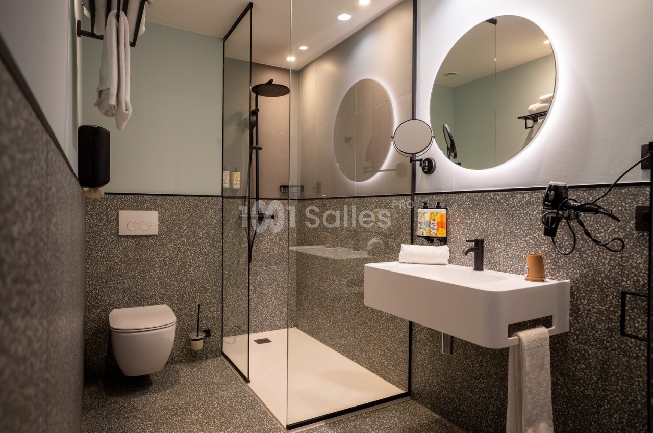 Salle de bain moderne avec douche à l'italienne, lavabo suspendu, miroir rond et toilettes suspendues.