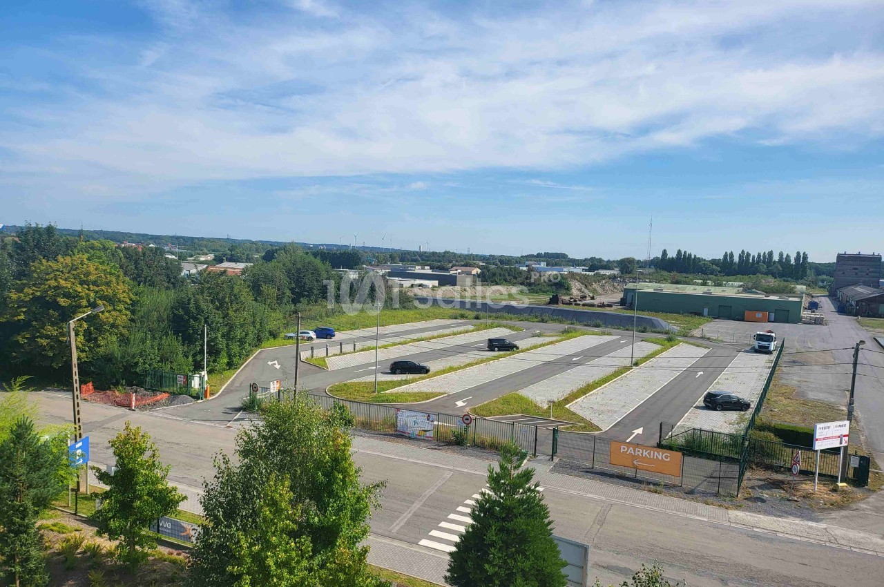 Vue aérienne d'un parking vide entouré de végétation, avec quelques voitures stationnées et un ciel dégagé.