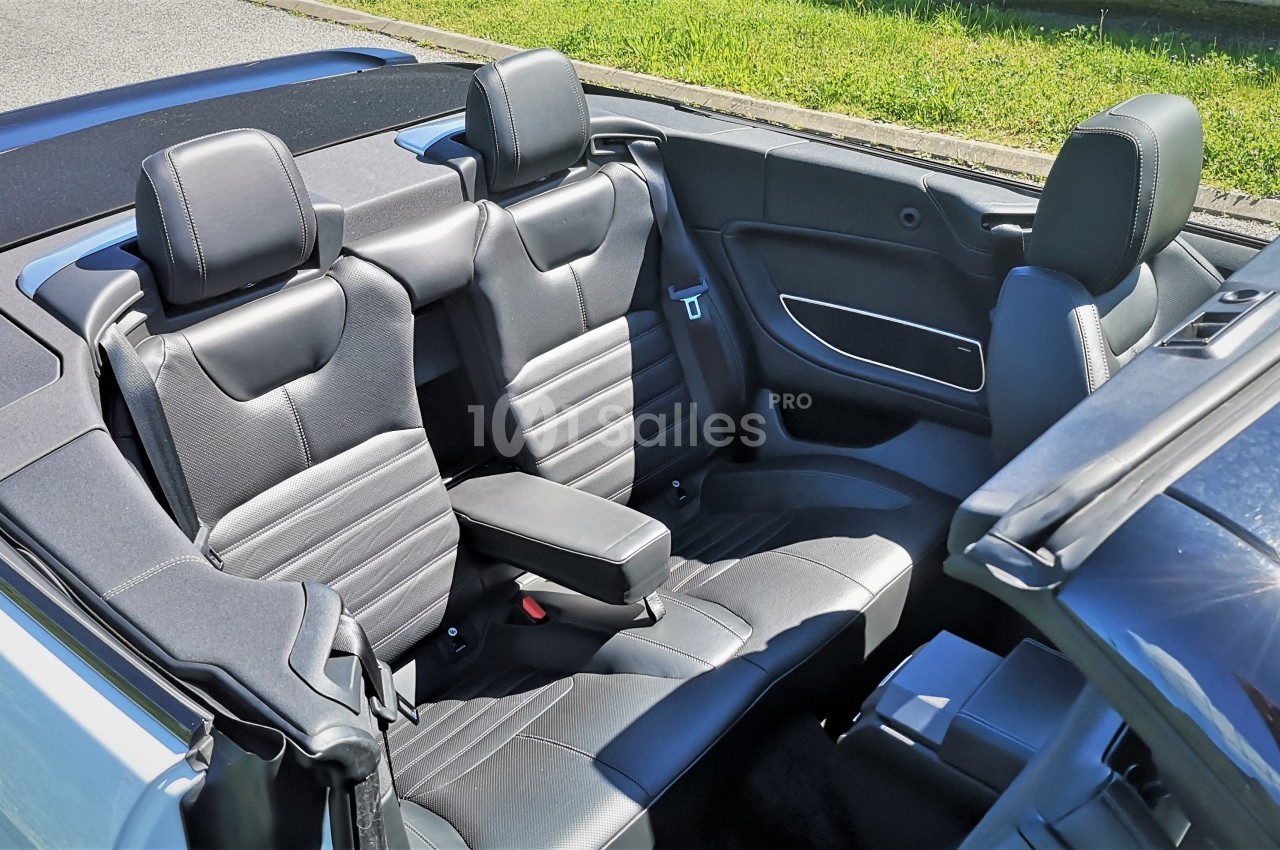 Intérieur d'une voiture décapotable avec sièges en cuir noir et accoudoir central, sous un éclairage naturel.