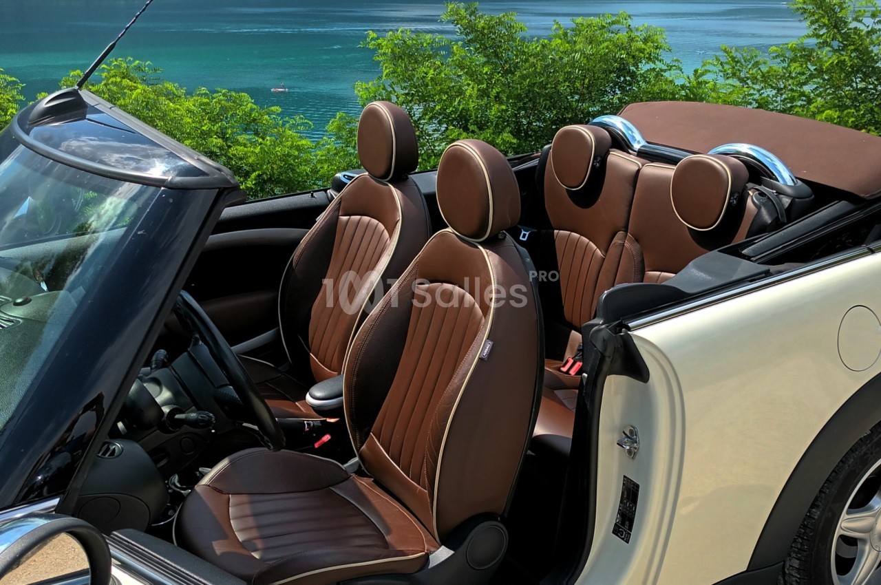 Voiture décapotable blanche avec intérieur en cuir marron, stationnée près d'un lac entouré de verdure.