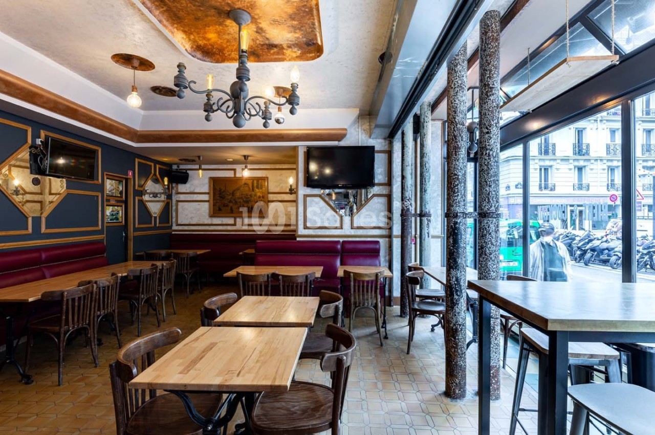 Salle de restaurant lumineuse avec tables en bois, chaises assorties, décorations murales et grandes fenêtres donnant sur la…