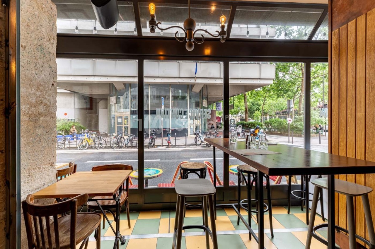 Intérieur d'un café avec des tables en bois, vue sur une rue avec des vélos et un bâtiment moderne à travers une baie vitrée.