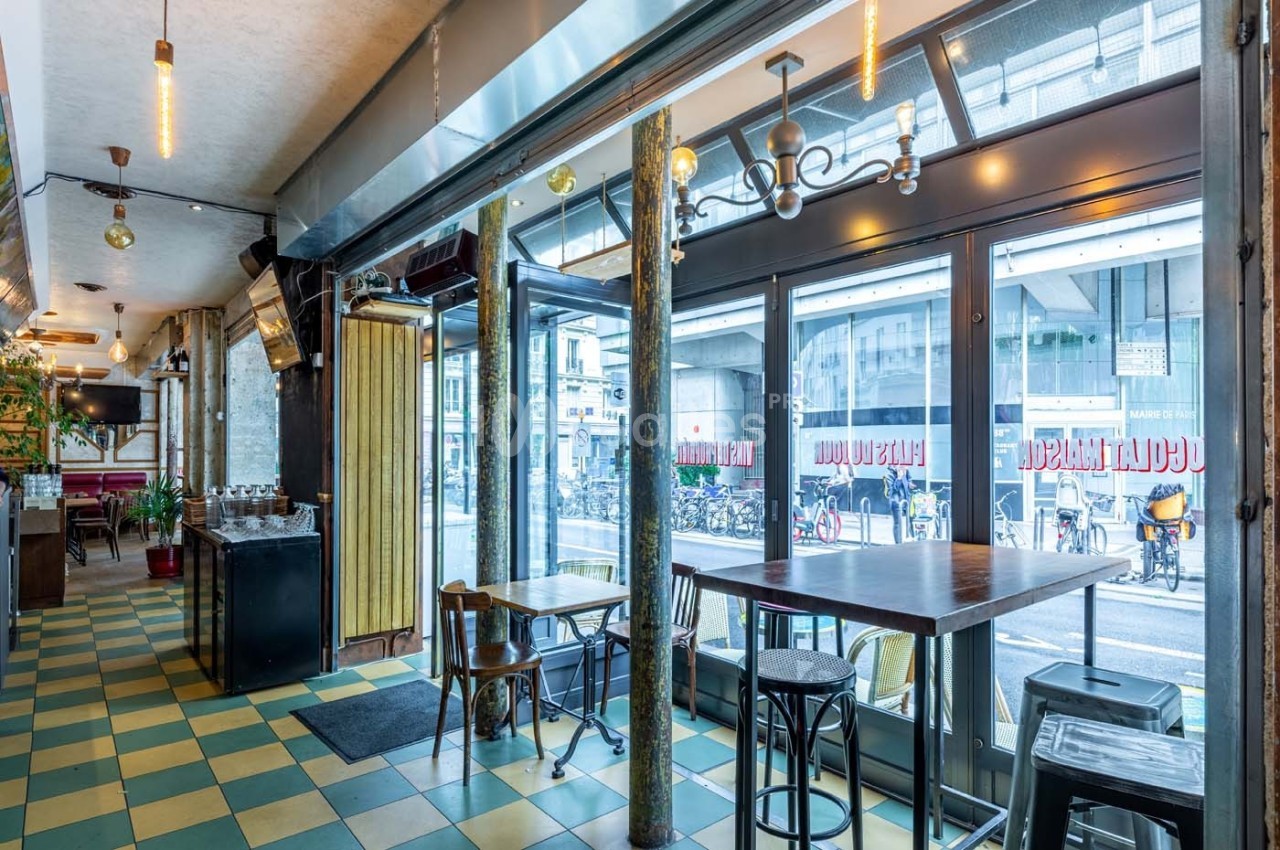Intérieur d'un café lumineux avec grandes baies vitrées donnant sur une rue urbaine et des rangées de vélos.
