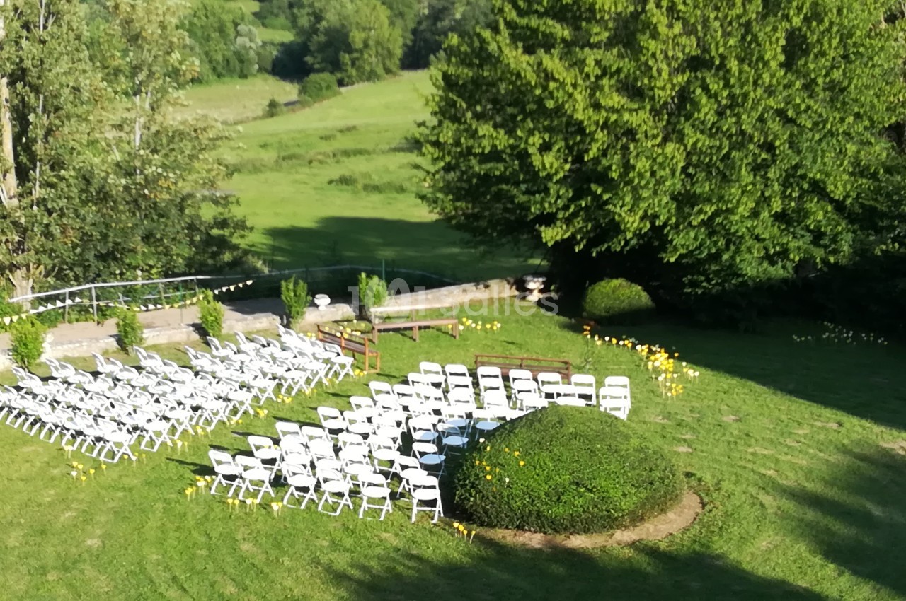 Chaises blanches disposées en extérieur sur une pelouse pour un événement, entourées d'arbres et de verdure.