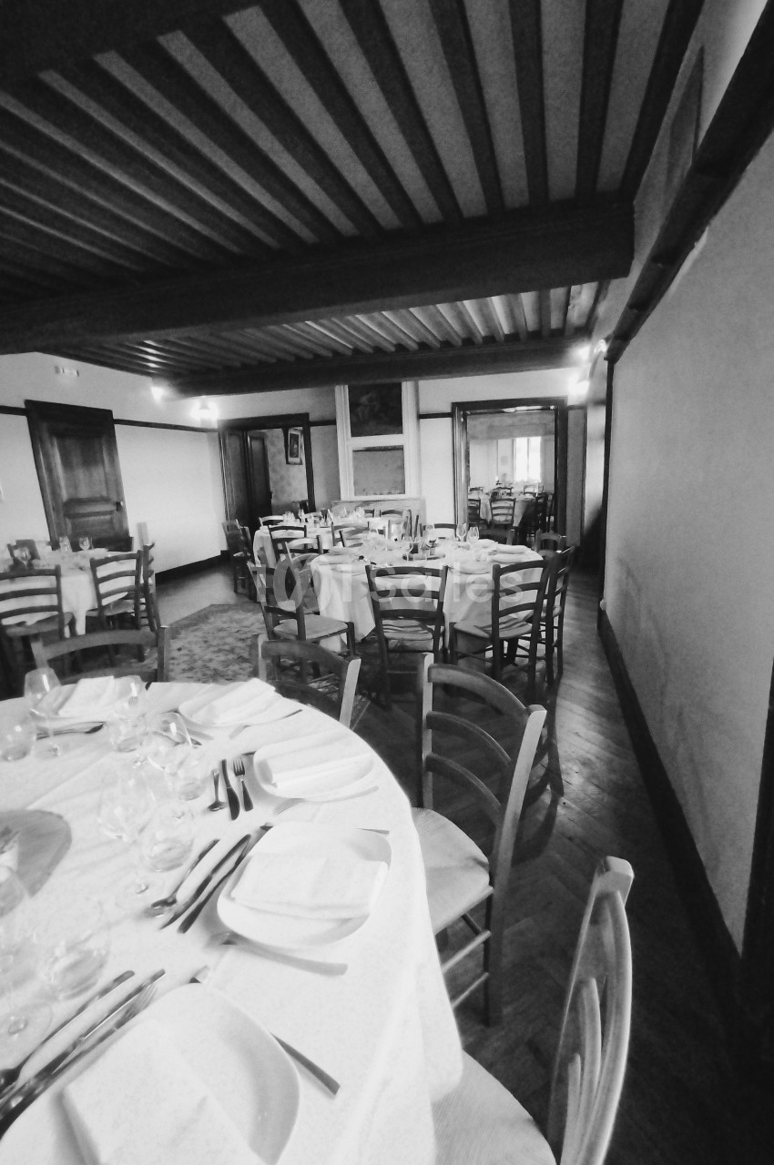 Salle de restaurant avec tables rondes dressées, nappes blanches, chaises en bois et éclairage tamisé.
