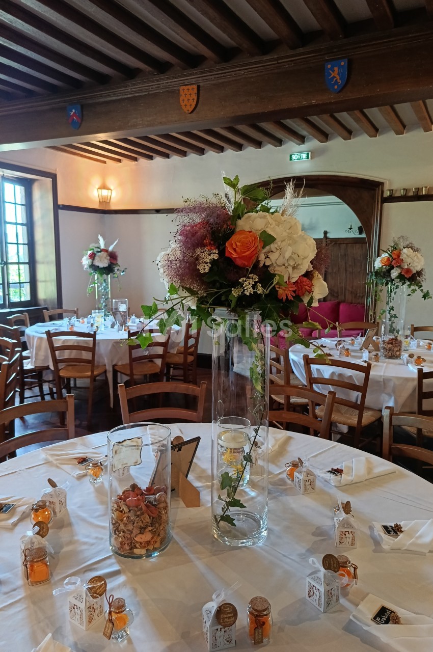 Salle de réception décorée avec des tables dressées, ornées de bouquets de fleurs et de petits cadeaux.