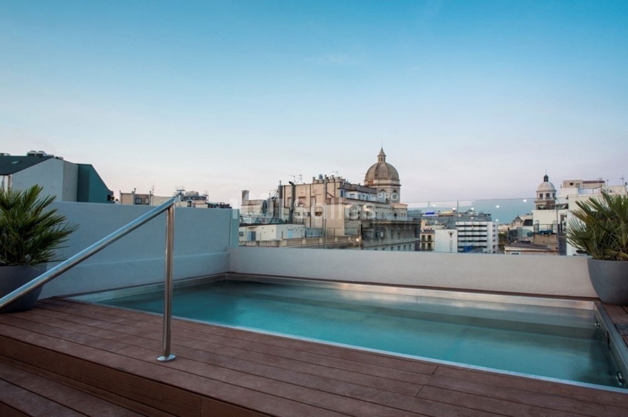 Piscine sur une terrasse en bois avec vue sur des bâtiments urbains et un ciel dégagé en arrière-plan.