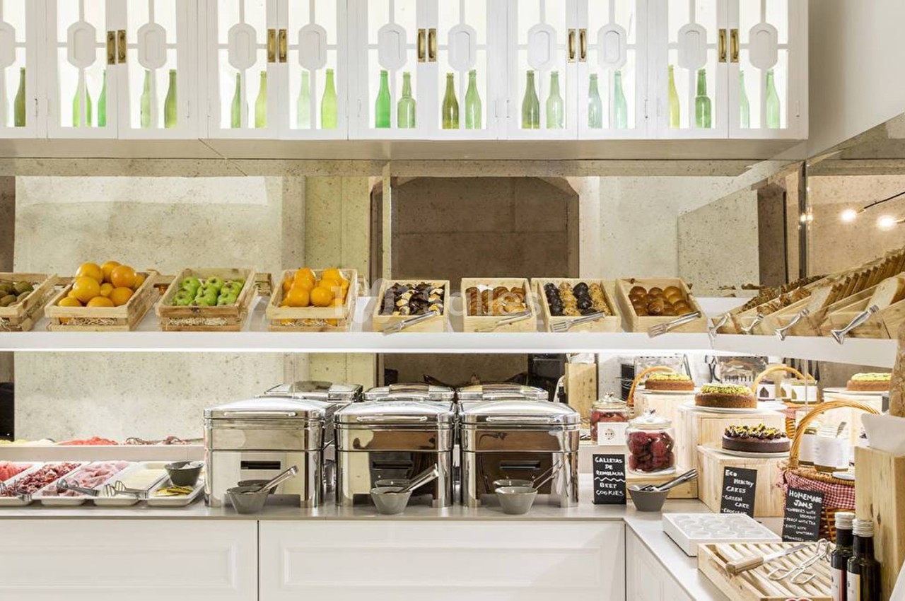 Buffet de petit-déjeuner avec fruits, viennoiseries, pains, plats chauds et boissons disposés sur un comptoir lumineux.