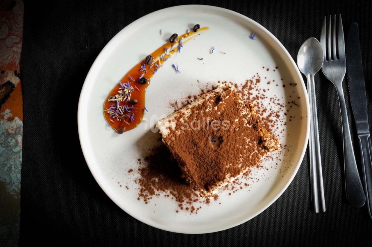 Dessert au cacao saupoudré, accompagné d'une sauce caramel décorée de fleurs et servi sur une assiette blanche.