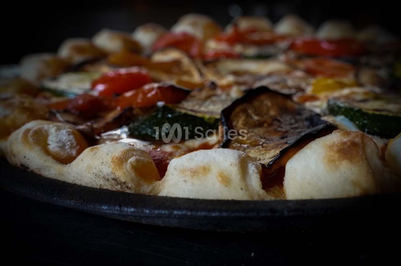 Pizza garnie de légumes grillés, notamment courgettes, aubergines et poivrons, sur une pâte dorée et moelleuse.