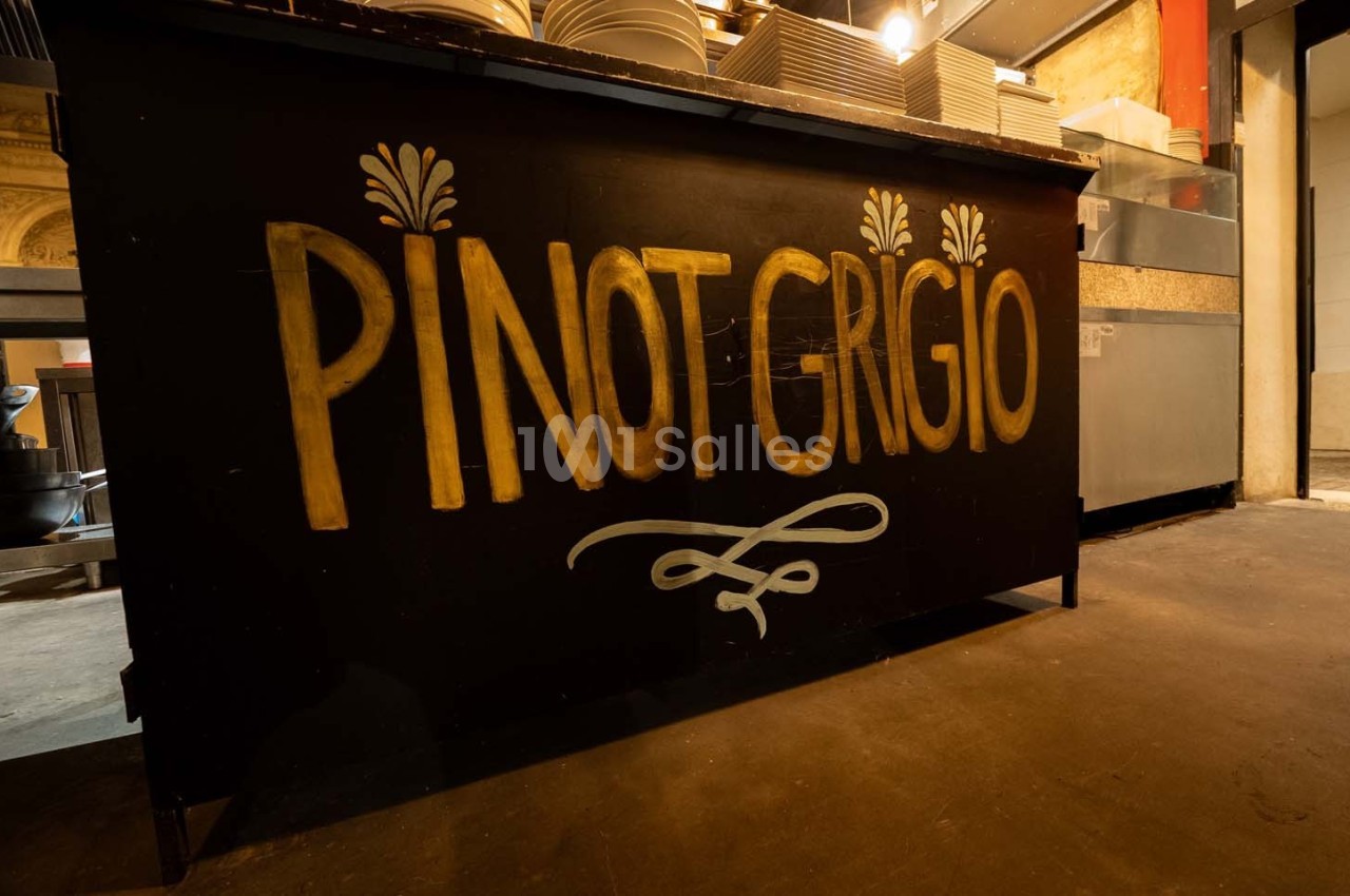 Comptoir noir avec l'inscription ’Pinot Grigio’ en lettres dorées, situé dans un espace intérieur avec vaisselle en arrière…