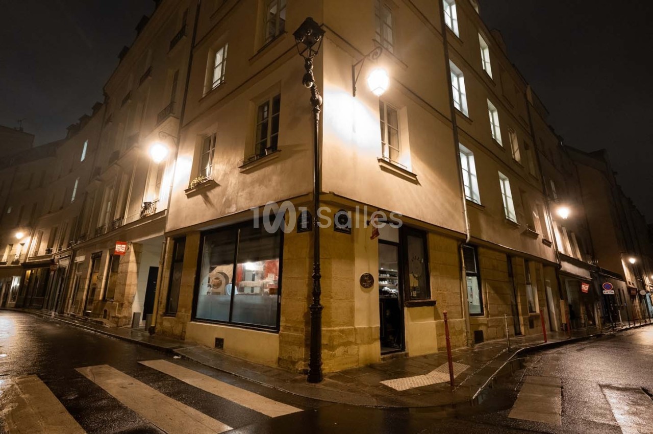Coin de rue parisienne la nuit, éclairé par des lampadaires, avec des bâtiments anciens et des fenêtres illuminées.