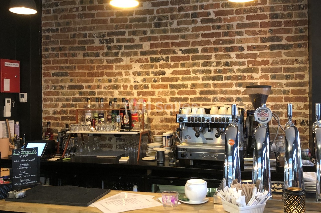 Comptoir de café avec machine à expresso, tireuses à bière, tasses et mur en briques en arrière-plan.
