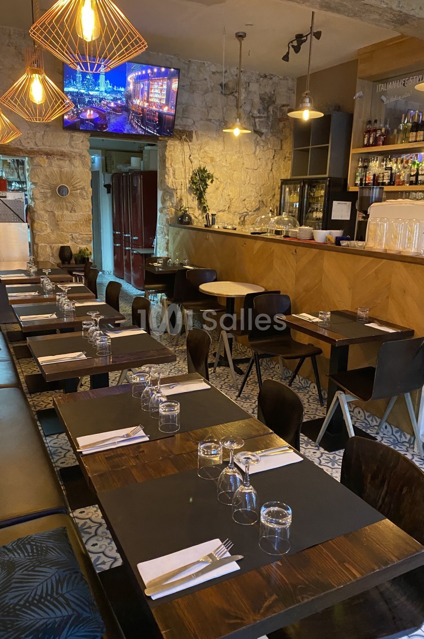 Salle de restaurant avec tables en bois dressées, bar en arrière-plan et éclairage chaleureux.