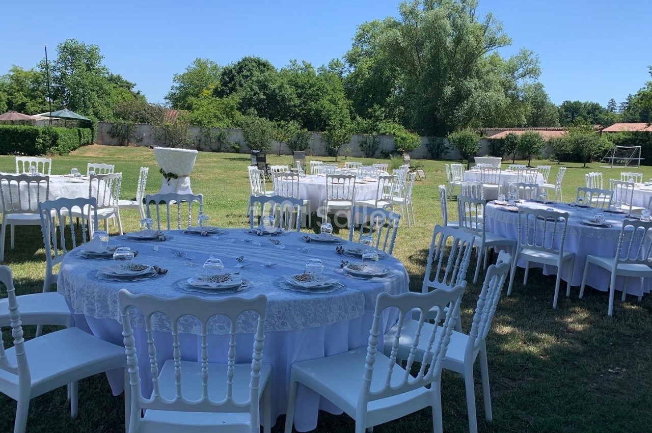 Tables rondes dressées avec nappes blanches et chaises disposées en extérieur sur une pelouse, par une journée ensoleillée.
