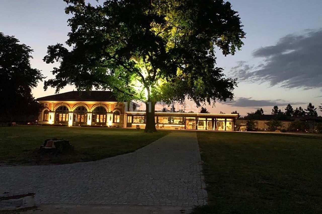 Allée pavée menant à un bâtiment illuminé sous un grand arbre au crépuscule.