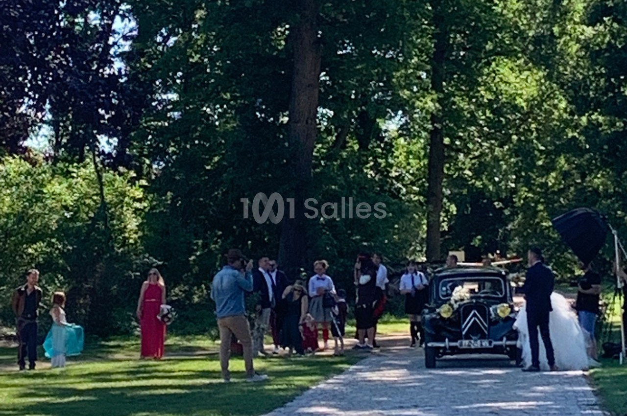 Un groupe de personnes rassemblé près d'une voiture ancienne décorée, dans un parc verdoyant.