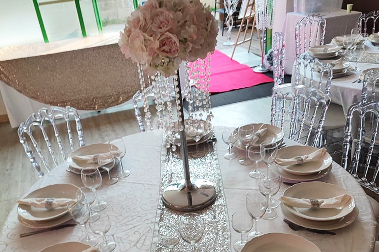 Table ronde décorée pour un événement, avec nappes blanches, vaisselle élégante et centre de table floral rose.