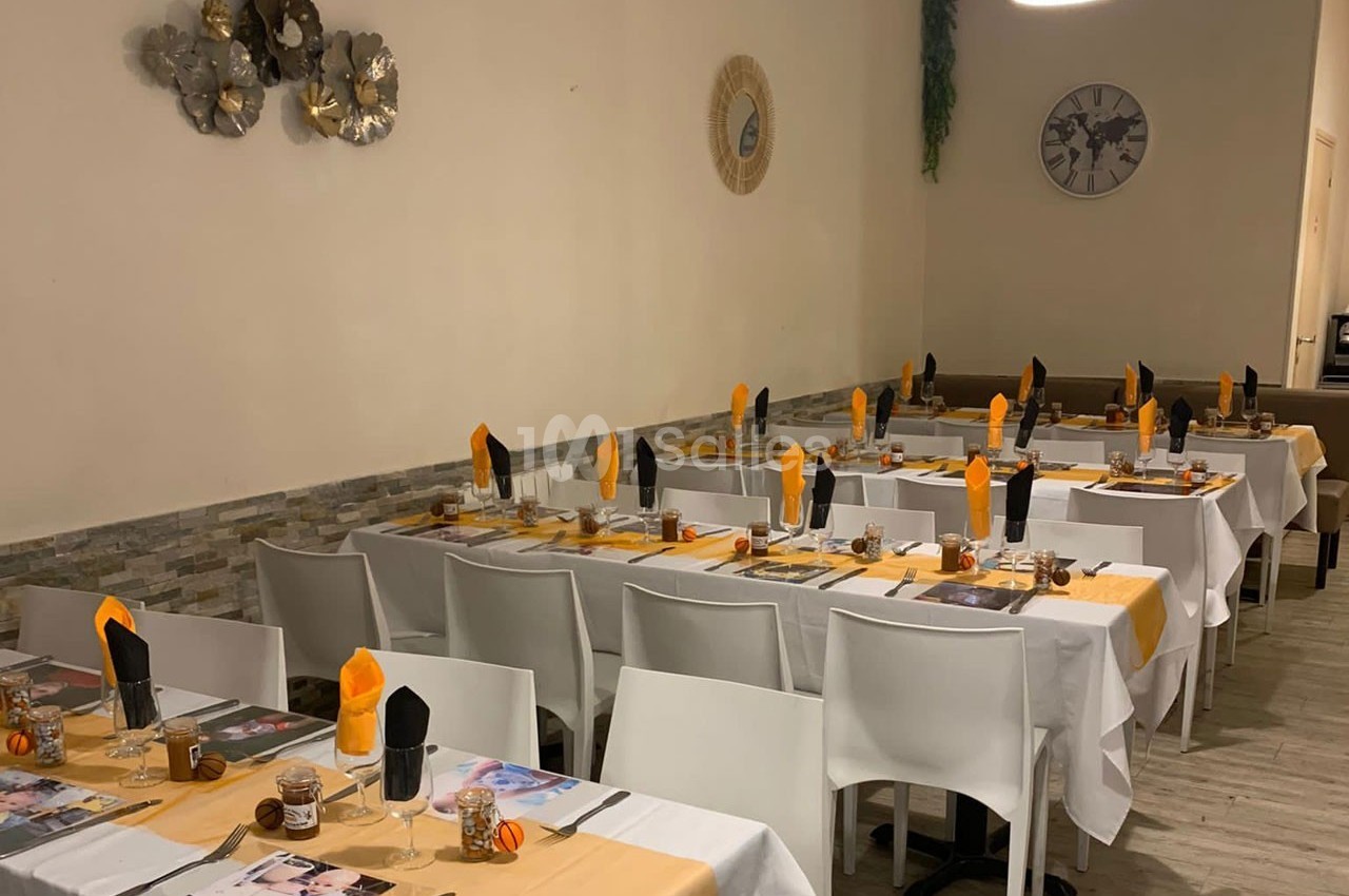 Salle de restaurant avec tables dressées, nappes blanches et jaunes, serviettes orange et noires, décor sobre.