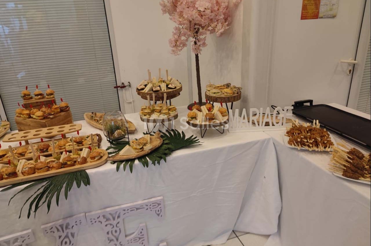 Buffet de réception avec assortiments de bouchées salées, décoré de feuilles tropicales et d'un arbre fleuri rose.