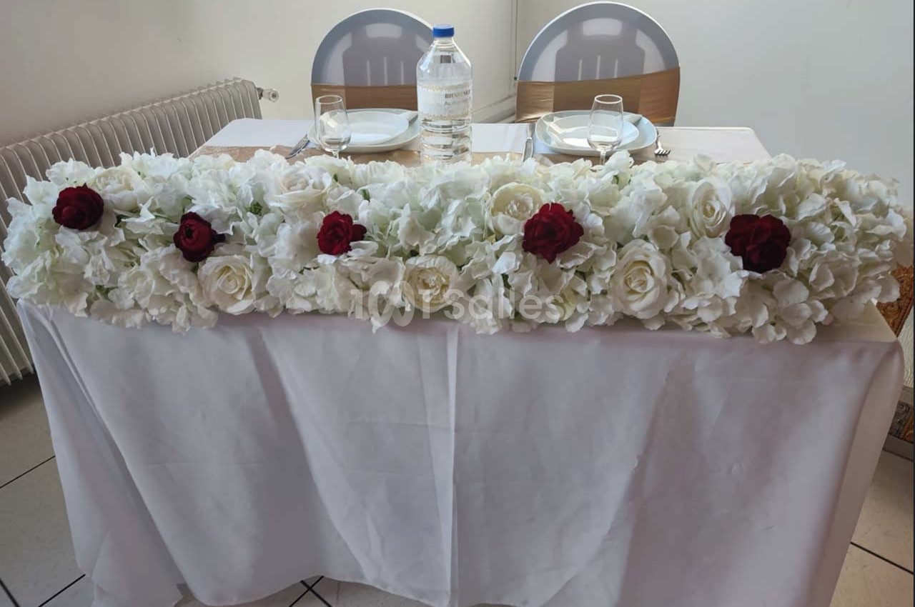 Décoration florale blanche et rouge ornant une table dressée avec deux chaises en arrière-plan.