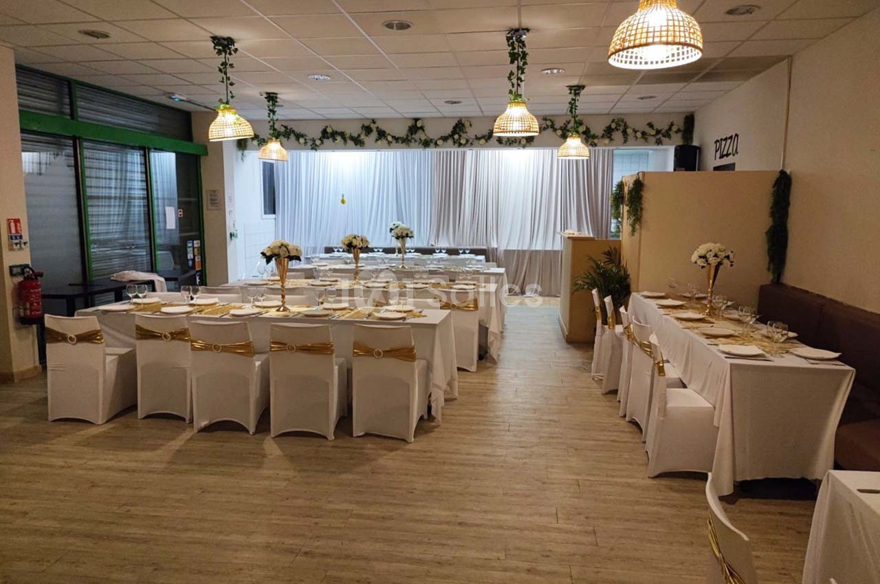 Salle de réception décorée avec des tables dressées, nappes blanches et ornements dorés, prête pour un événement.