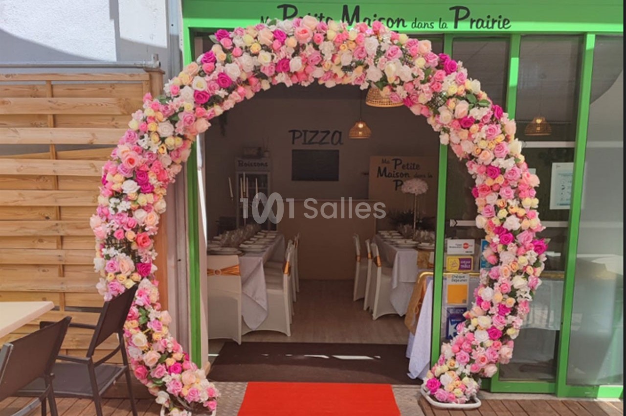 Arc floral coloré encadrant l'entrée d'un restaurant avec une table dressée visible à l'intérieur.