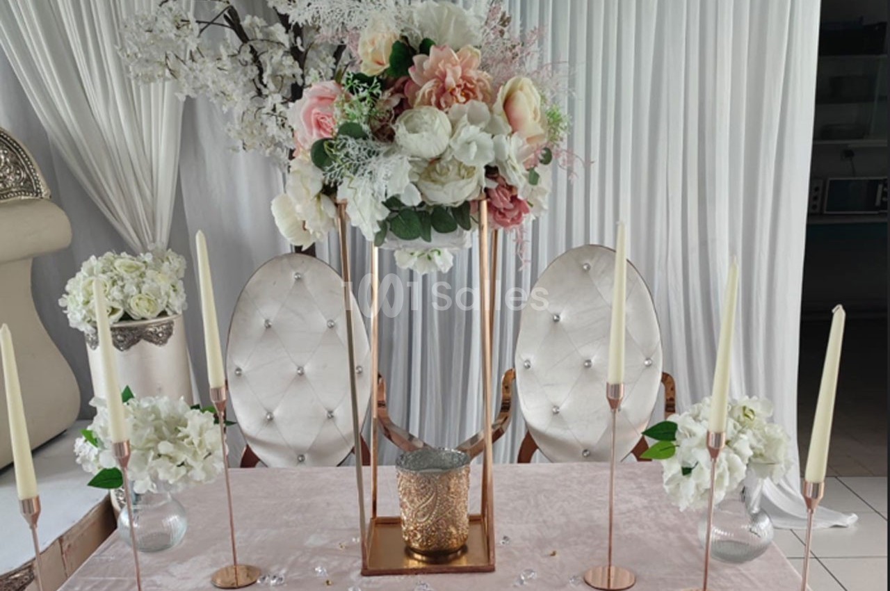 Décoration de table élégante avec fleurs blanches et roses, chandeliers dorés et chaises capitonnées blanches.