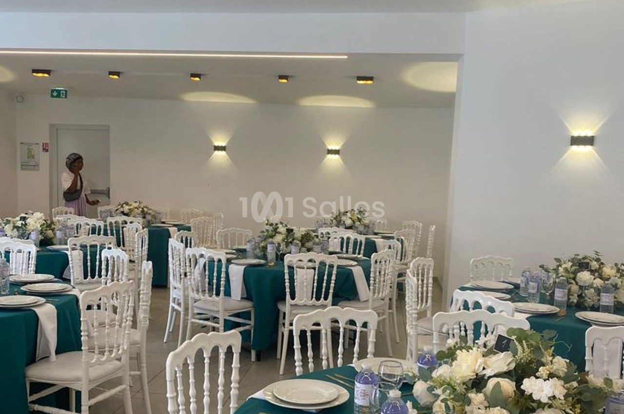 Salle de réception décorée avec des tables dressées, nappes vertes, chaises blanches et arrangements floraux.