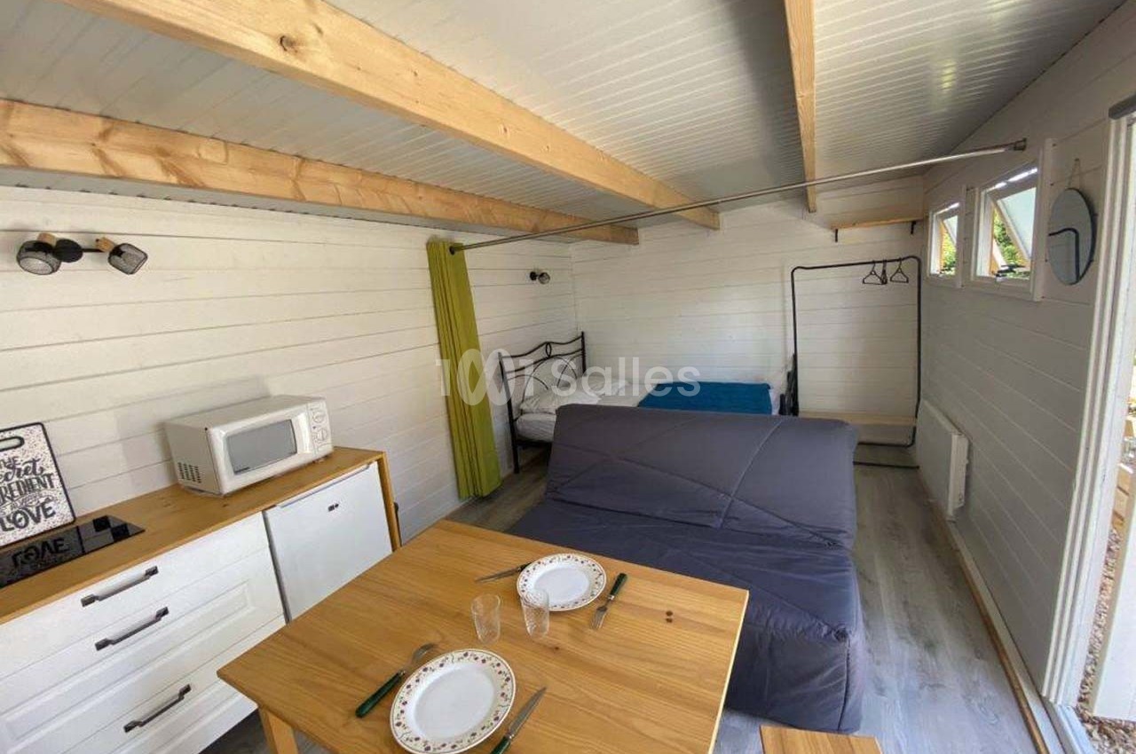 Intérieur d'un petit studio en bois avec lit, canapé, table à manger, kitchenette et lumière naturelle.
