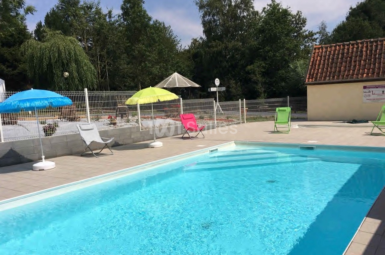 Piscine extérieure avec eau claire, entourée de chaises longues colorées et de parasols, dans un cadre arboré.