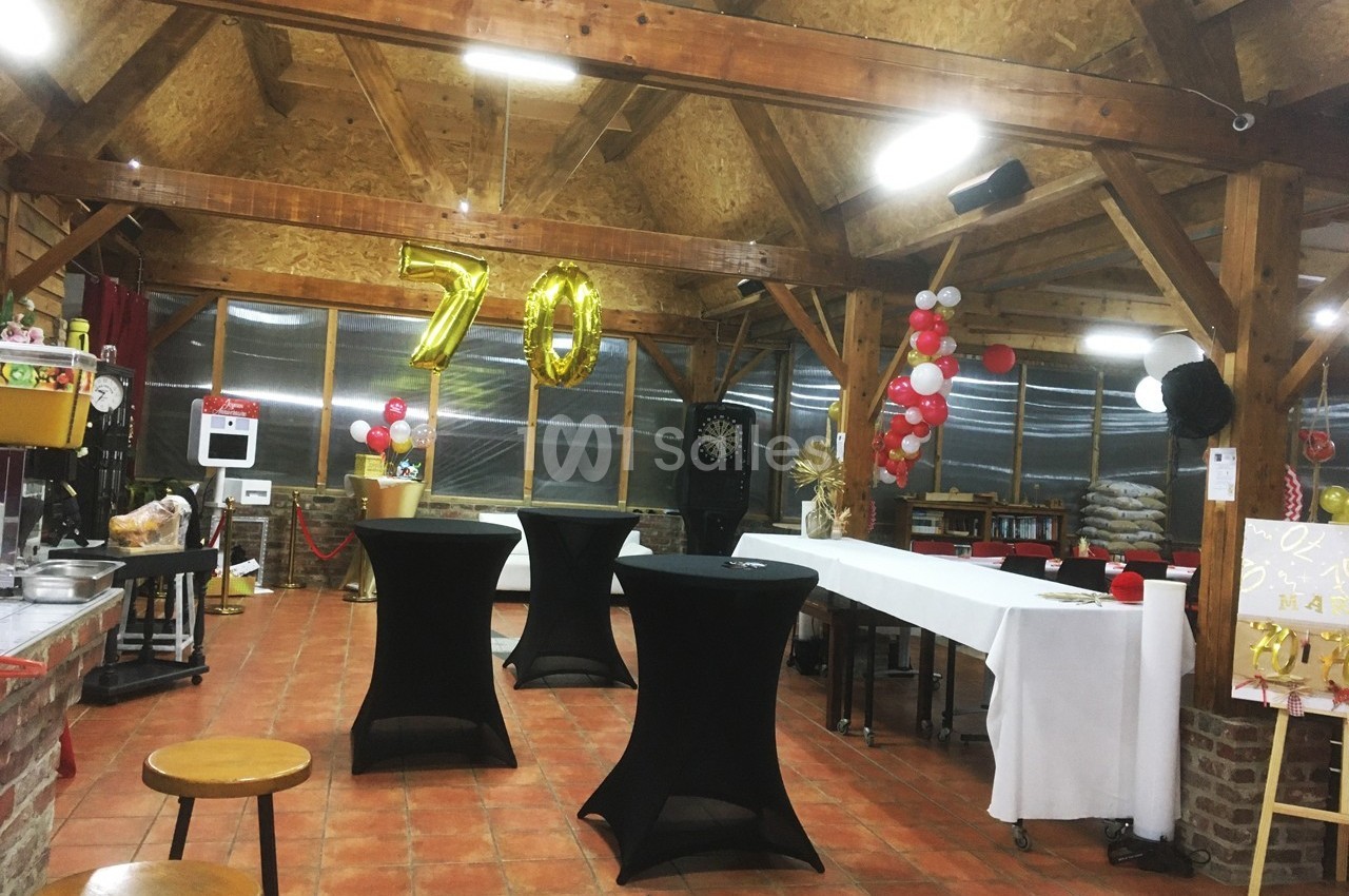 Salle décorée pour un 70e anniversaire avec ballons dorés, tables hautes noires et guirlandes rouges et blanches.