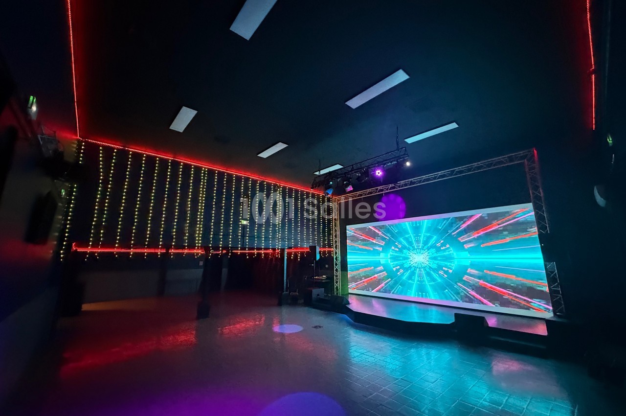 Salle sombre avec écran géant affichant des effets lumineux colorés et murs décorés de guirlandes LED.