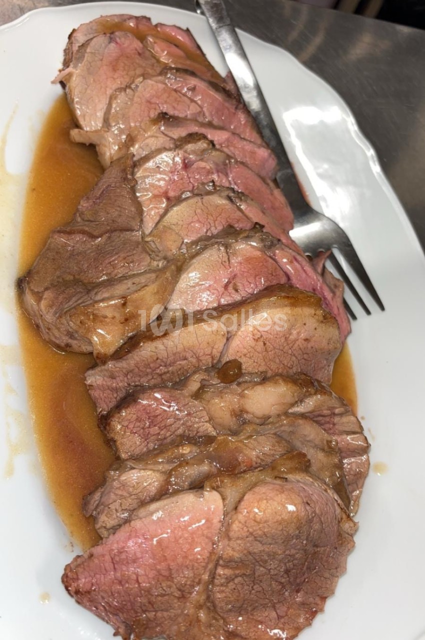 Tranches de viande rôtie servies sur un plat blanc avec une sauce et une fourchette en arrière-plan.