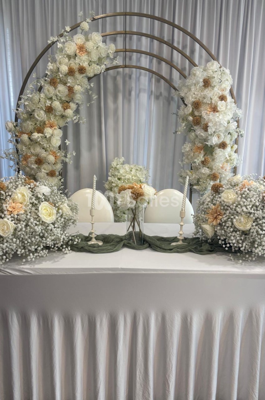 Table décorée pour un mariage avec des fleurs blanches et beige, bougies et arche florale en arrière-plan.