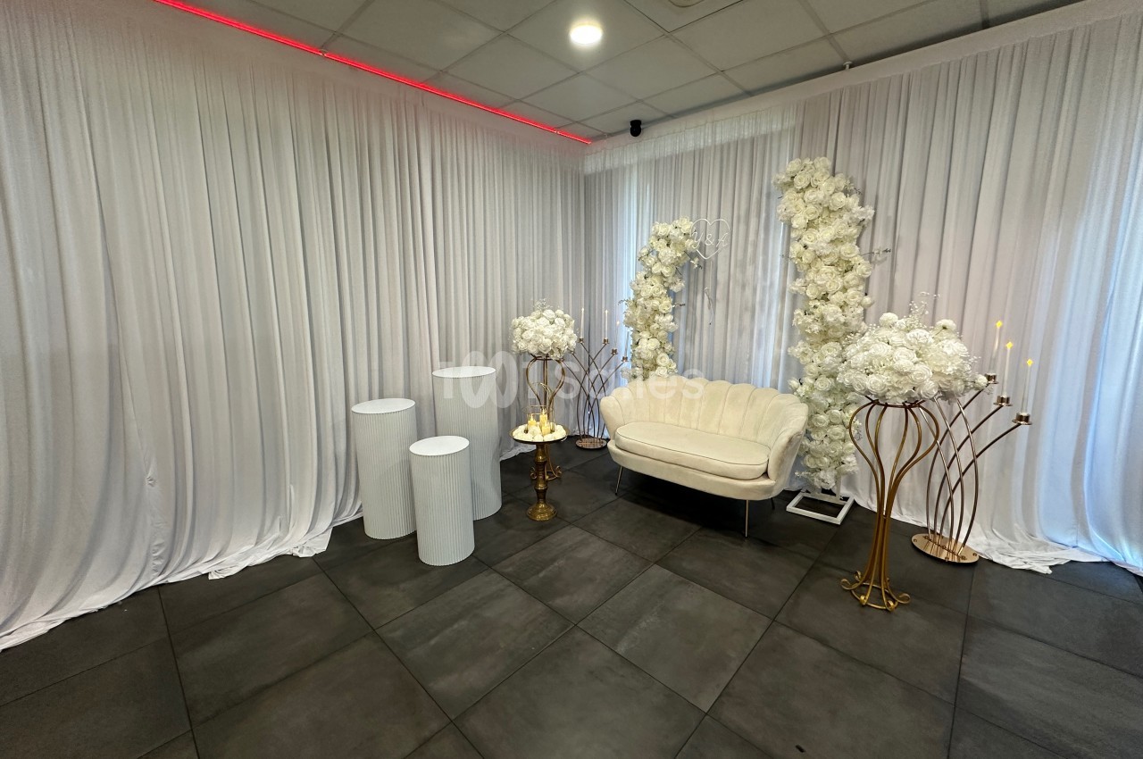 Salle décorée avec des rideaux blancs, un canapé, des colonnes, des fleurs blanches et des chandeliers dorés.