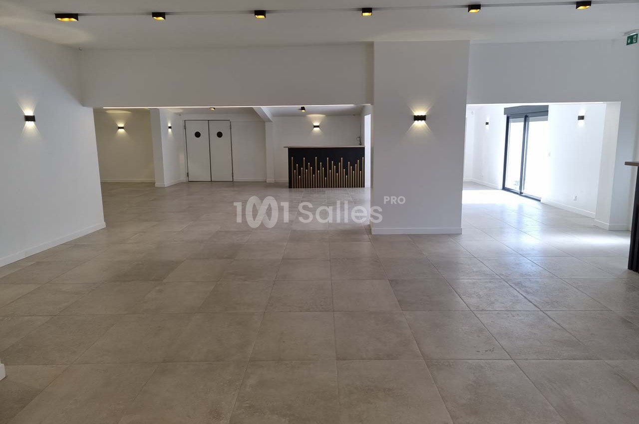 Salle spacieuse et lumineuse avec sol en carrelage beige, murs blancs et éclairage mural moderne.