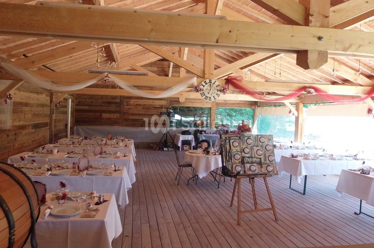 Salle en bois décorée pour un événement, avec des tables dressées et un chevalet exposant une toile.