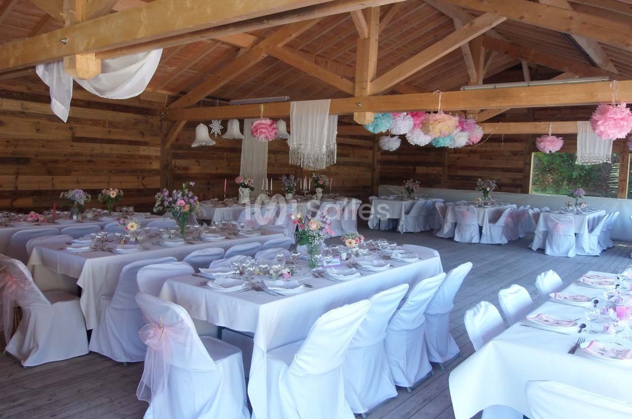 Salle de réception en bois décorée avec des tables dressées, nappes blanches et suspensions colorées.