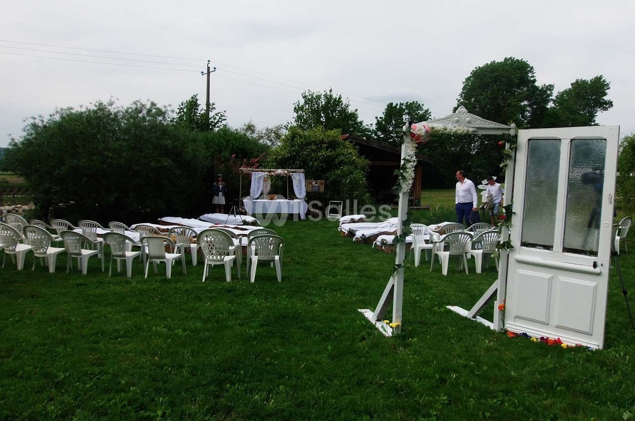 Chaises blanches disposées en extérieur sur une pelouse, face à une arche décorée pour une cérémonie.