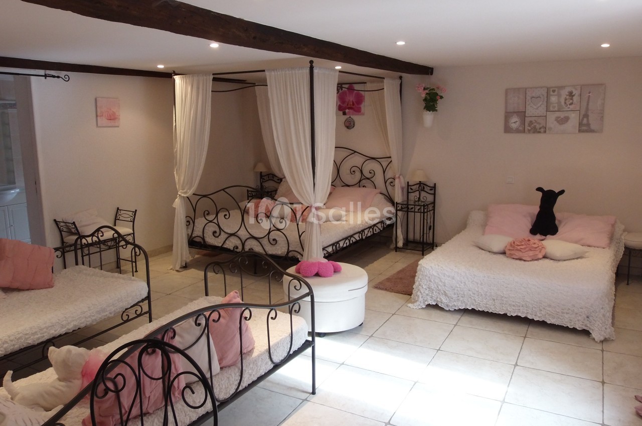 Chambre lumineuse avec lits à baldaquin, décorée dans des tons roses et blancs, poutres apparentes au plafond.
