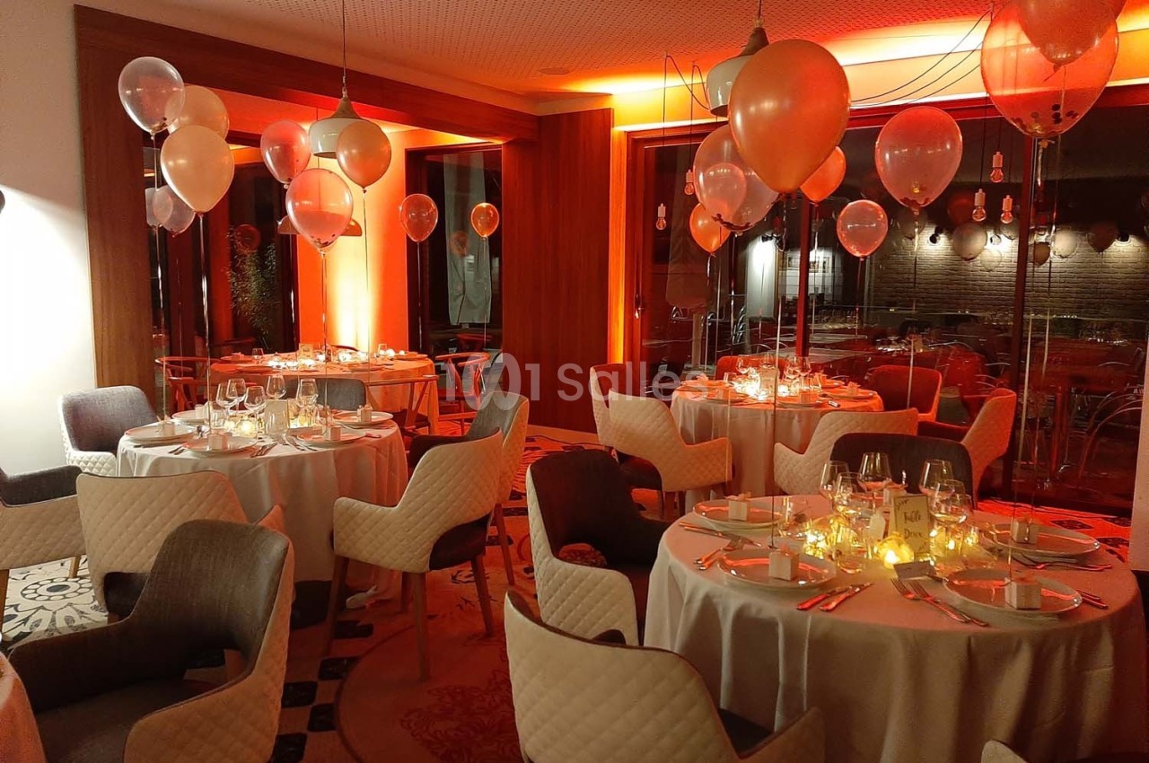 Salle de réception décorée avec des ballons et des lumières tamisées, tables dressées pour un dîner élégant.