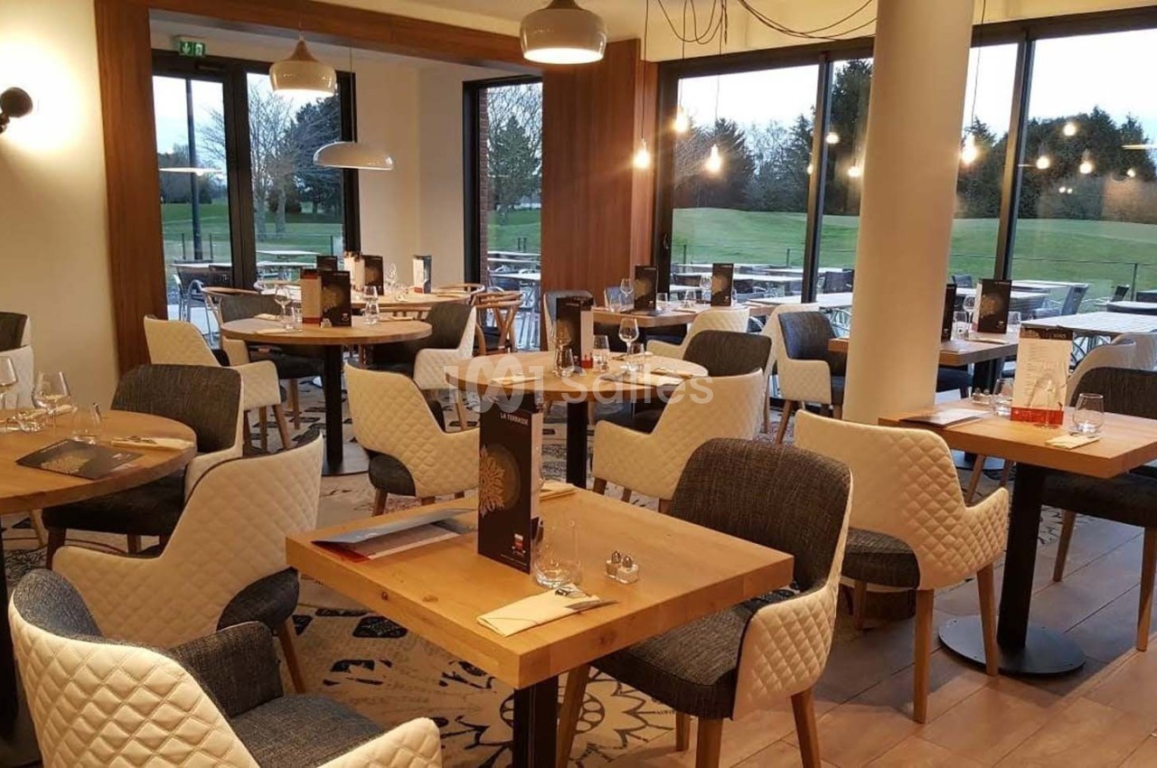 Salle de restaurant lumineuse avec tables en bois, chaises rembourrées et grandes baies vitrées donnant sur un espace…