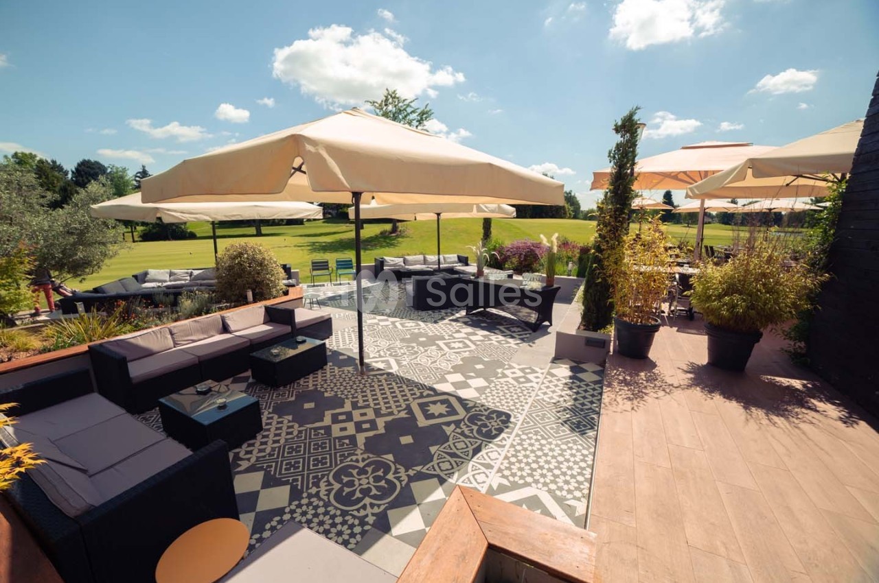 Terrasse aménagée avec canapés, tables basses, grands parasols et vue sur un jardin verdoyant par temps ensoleillé.
