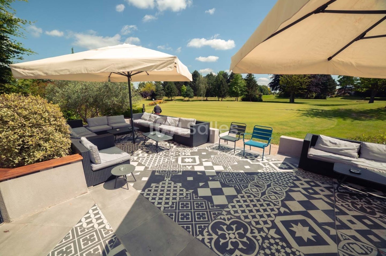 Terrasse aménagée avec mobilier de jardin, parasols et vue sur un grand espace vert parsemé d'arbres.