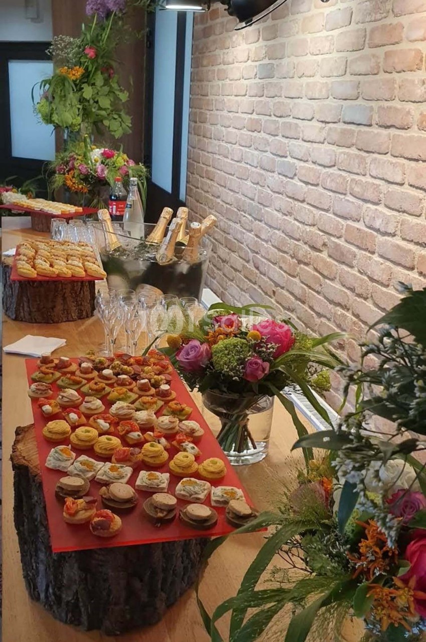 Plateau de bouchées apéritives variées sur une table en bois décorée de fleurs et de bouteilles de champagne.