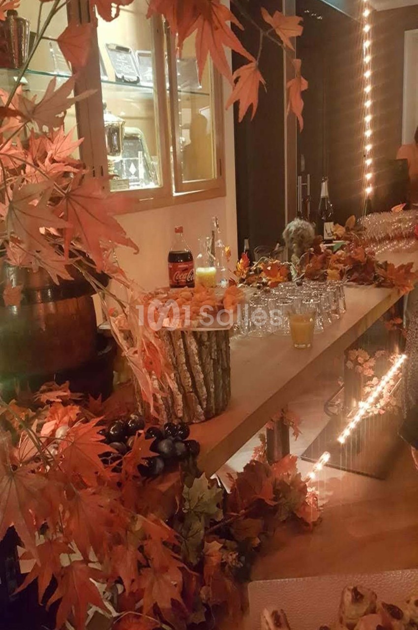 Table décorée sur le thème de l'automne avec feuilles rouges, boissons, verrerie et amuse-bouches dans un cadre chaleureux.