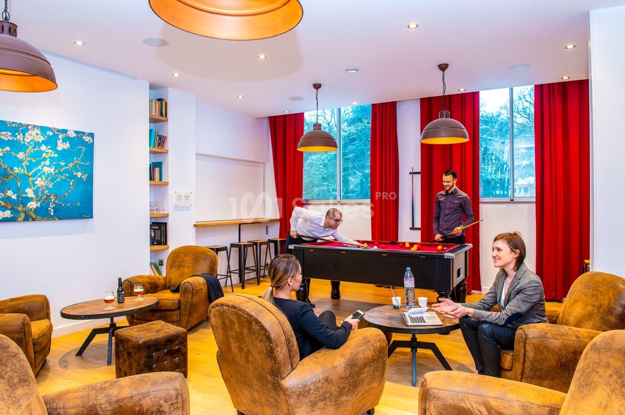 Des personnes discutent et jouent au billard dans un espace lumineux avec fauteuils, tables et décorations murales.
