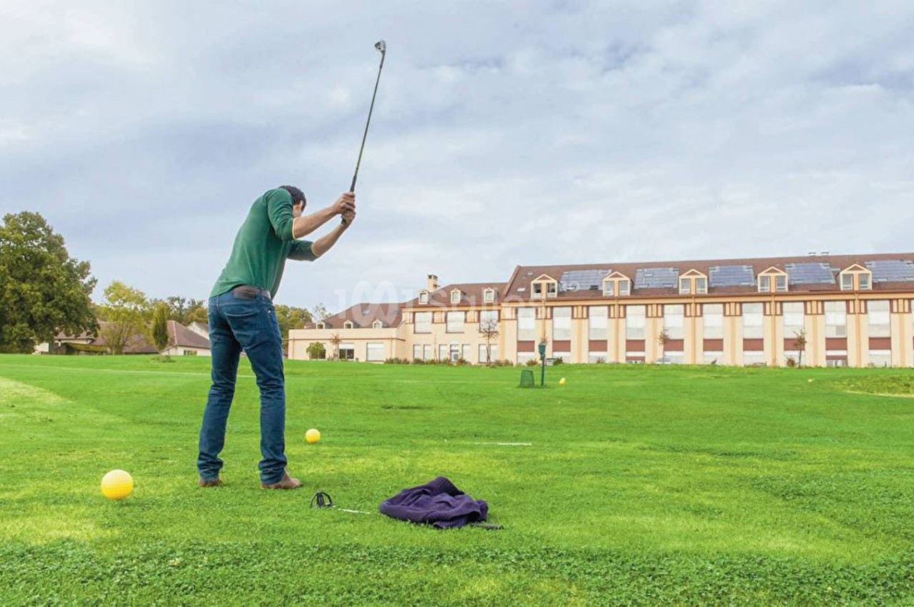 Un golfeur effectue un swing sur un terrain de golf, avec un bâtiment en arrière-plan.