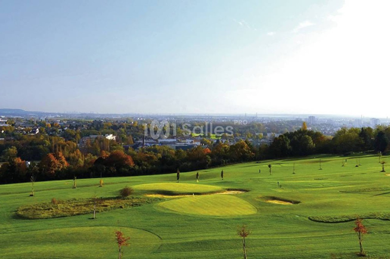Vue d'un terrain de golf verdoyant avec des arbres et une ville en arrière-plan sous un ciel dégagé.